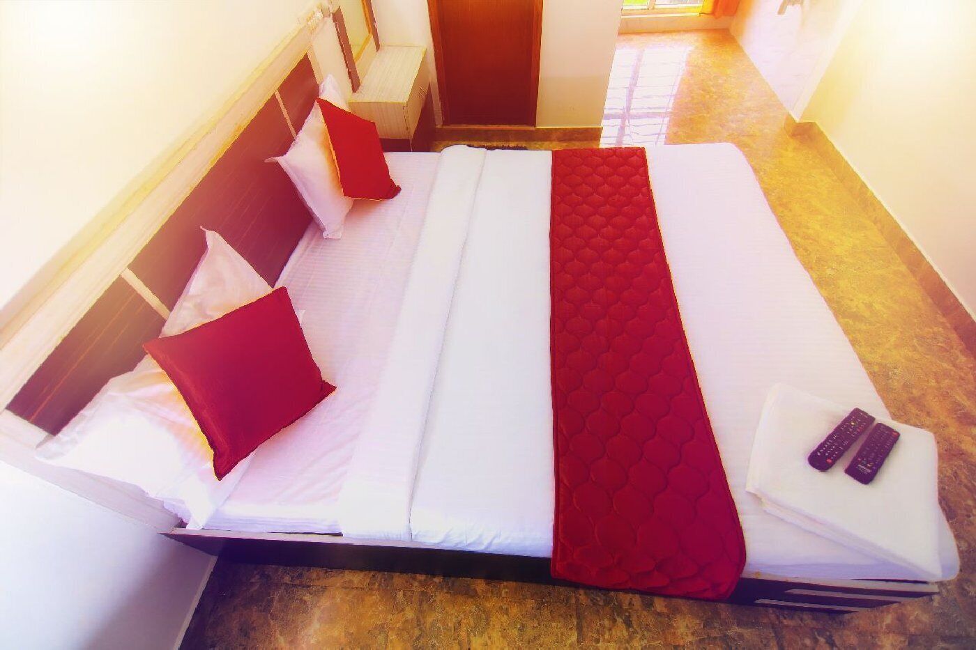 A hotel room with a bed, pillows, a blanket, and two remote controls on the bed.