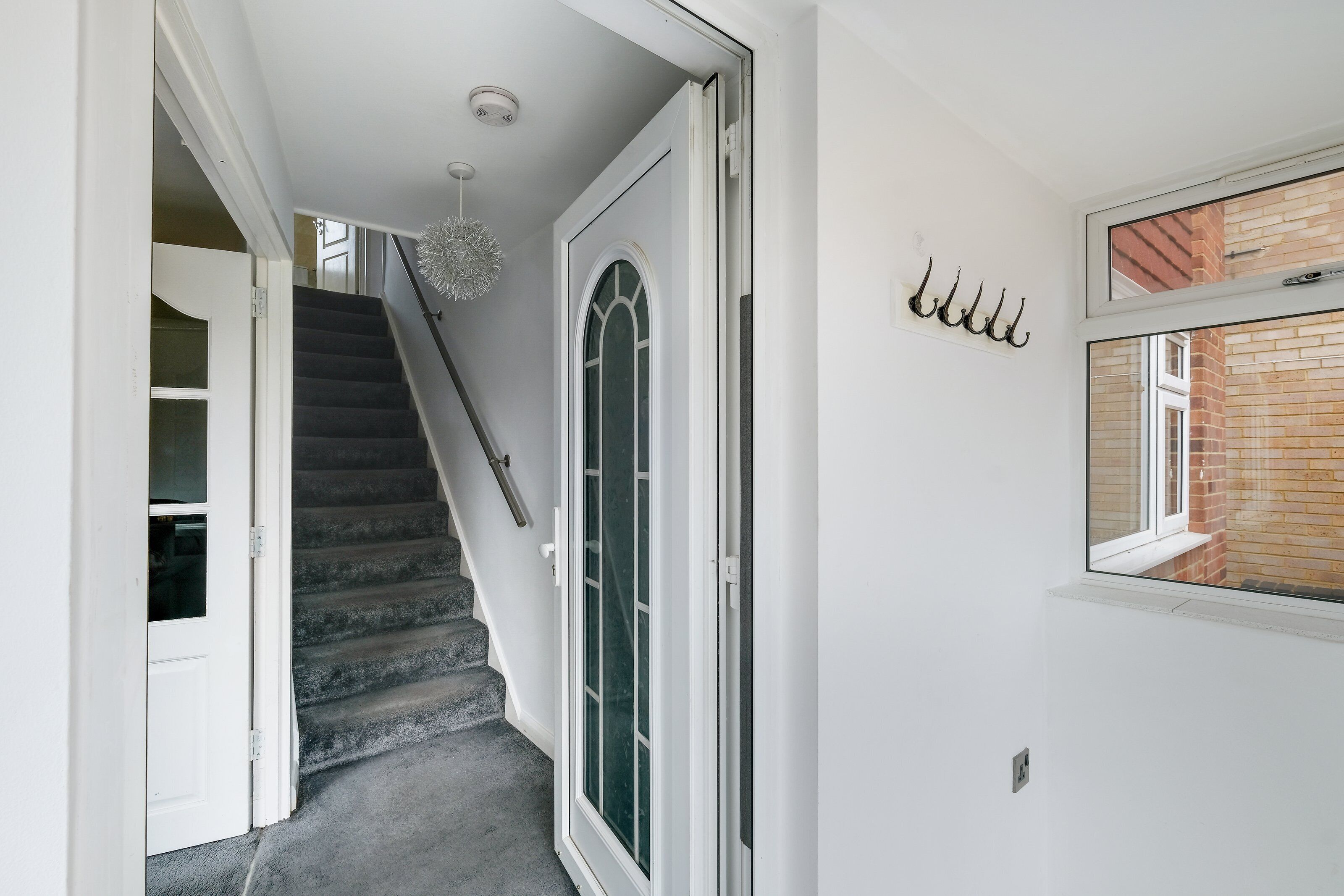 A staircase leading to a door with a glass panel, a hanging light fixture, and a window with a view of a brick building.