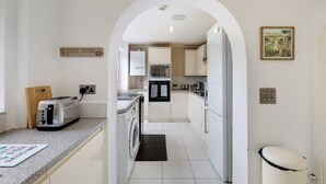 A modern kitchen with a toaster, washing machine, and a small dining area. -  Elegant 5BR Home with Free EV Charger, Garden and Parking (Slough)
