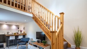 A modern living space with a wooden staircase, a kitchen area, a dining table, and a seating area with a sofa and chairs.