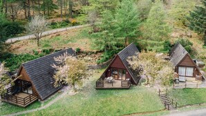 Deux petites cabanes aux toits inclinés, entourées d’une forêt dense. Chaque cabane possède une terrasse avec des meubles pour se détendre à l’extérieur.