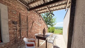 Een rustiek terras met een bakstenen muur, een houten tafel, twee rieten stoelen en uitzicht op het landschap.