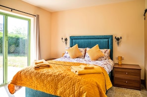 Une chambre à coucher avec un lit, deux tables de chevet, une fenêtre et une vue sur la verdure.