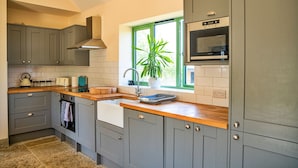 Una cucina con mobili grigi, un piano di lavoro in legno, un forno a microonde integrato e una finestra con una pianta.