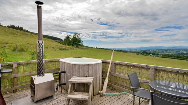 A wooden deck with a hot tub, a grill, and a table with chairs. - Chalet With Gleneagles Views, hot Tub, No Deposit (Auchterarder)