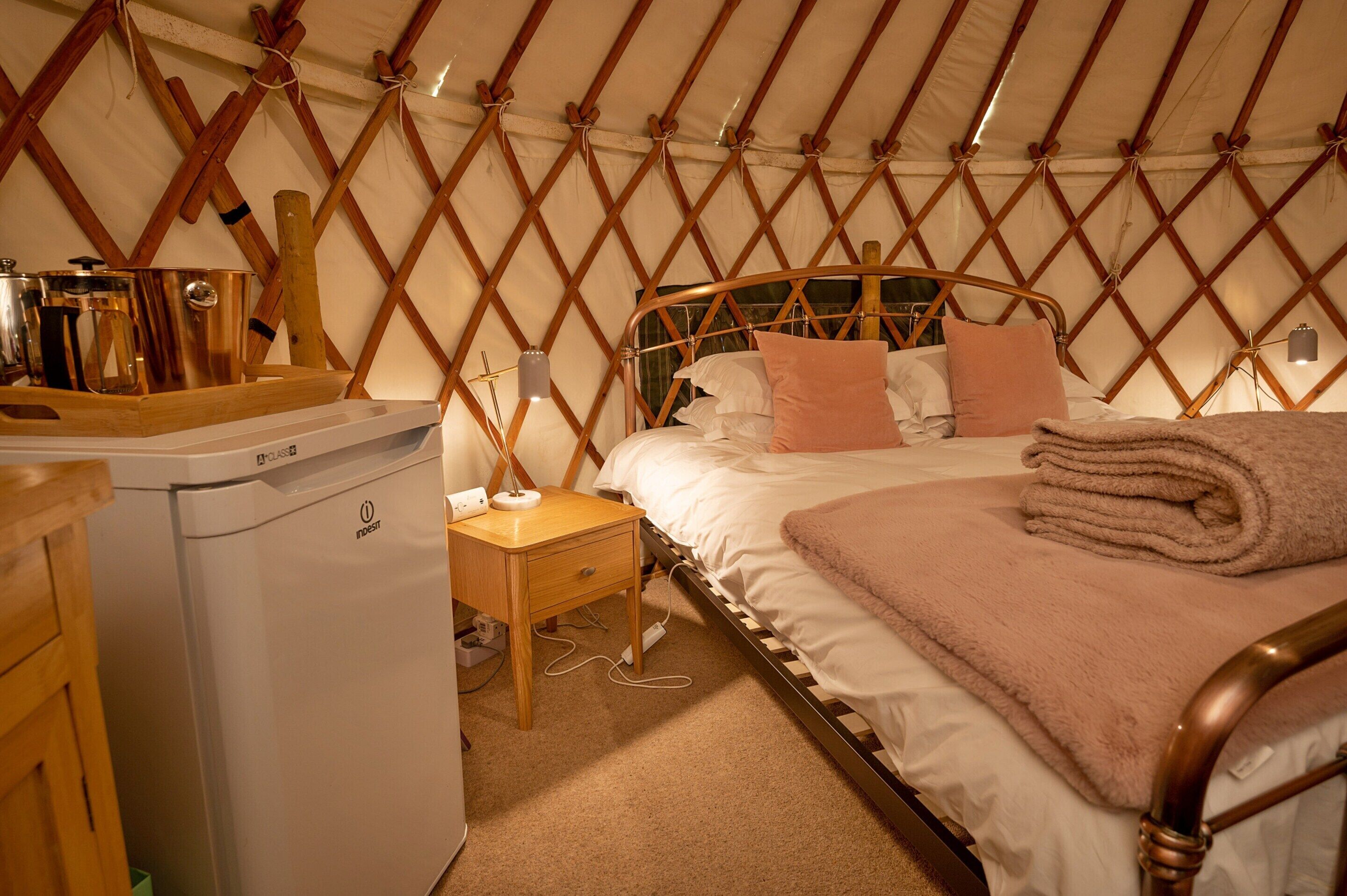 A cozy room with a bed, a wooden nightstand, a small table, and a white appliance.