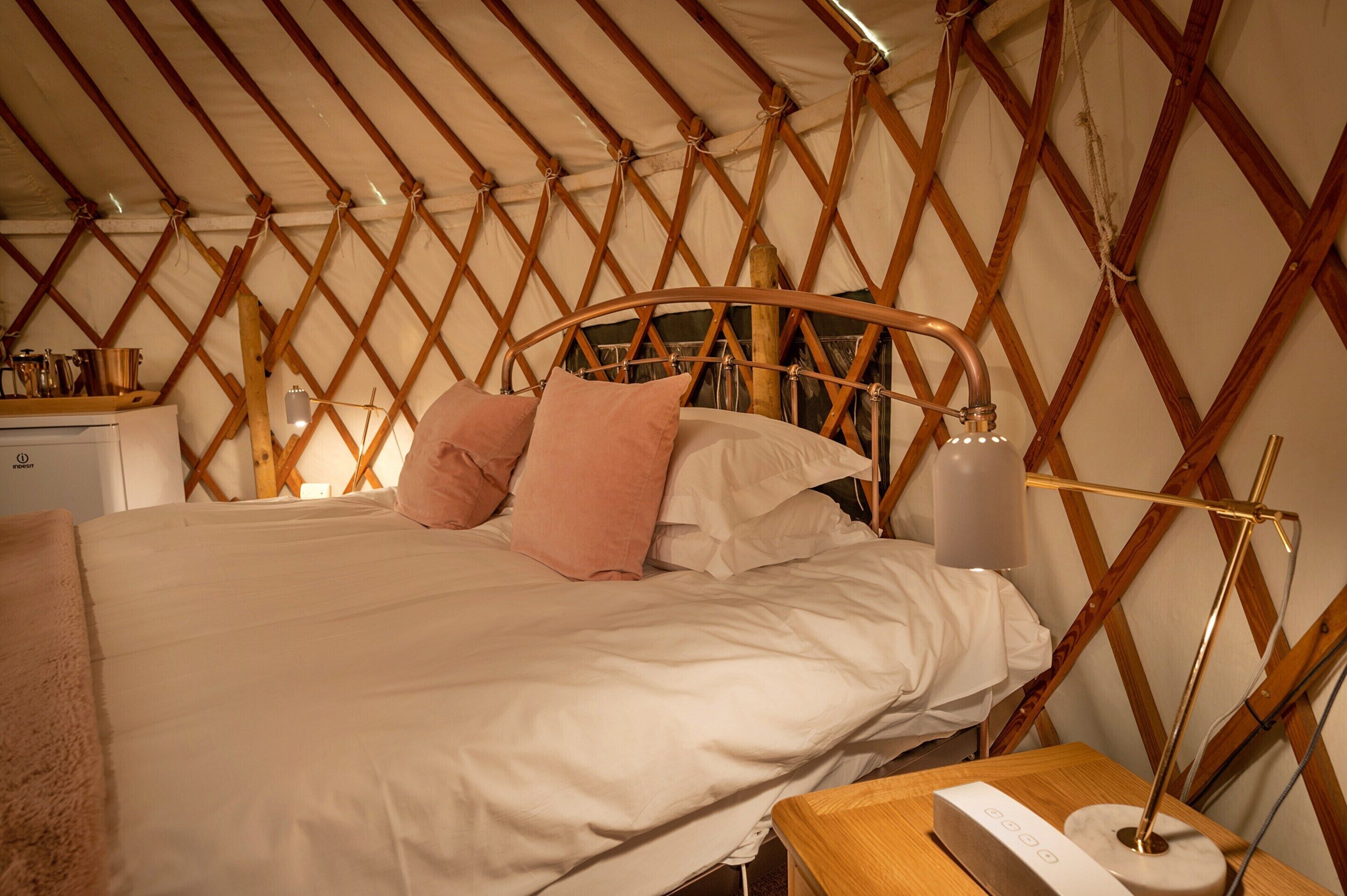 Una cama con estructura de madera, ropa de cama blanca y dos almohadas rosas.