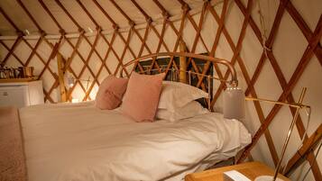 Una cama con estructura de madera, ropa de cama blanca y dos almohadas rosas.