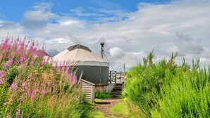 A yurt with a covered entrance, surrounded by lush greenery and flowering plants. - Chalet With Gleneagles Views, hot Tub, No Deposit (Auchterarder)