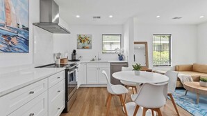 Une cuisine moderne avec des meubles blancs, un îlot central et un coin repas avec des chaises blanches.