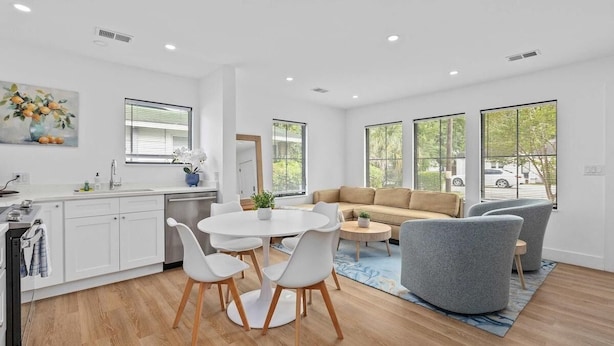 Une cuisine moderne avec des meubles blancs, une table à manger avec des chaises et une grande fenêtre équipée de stores.