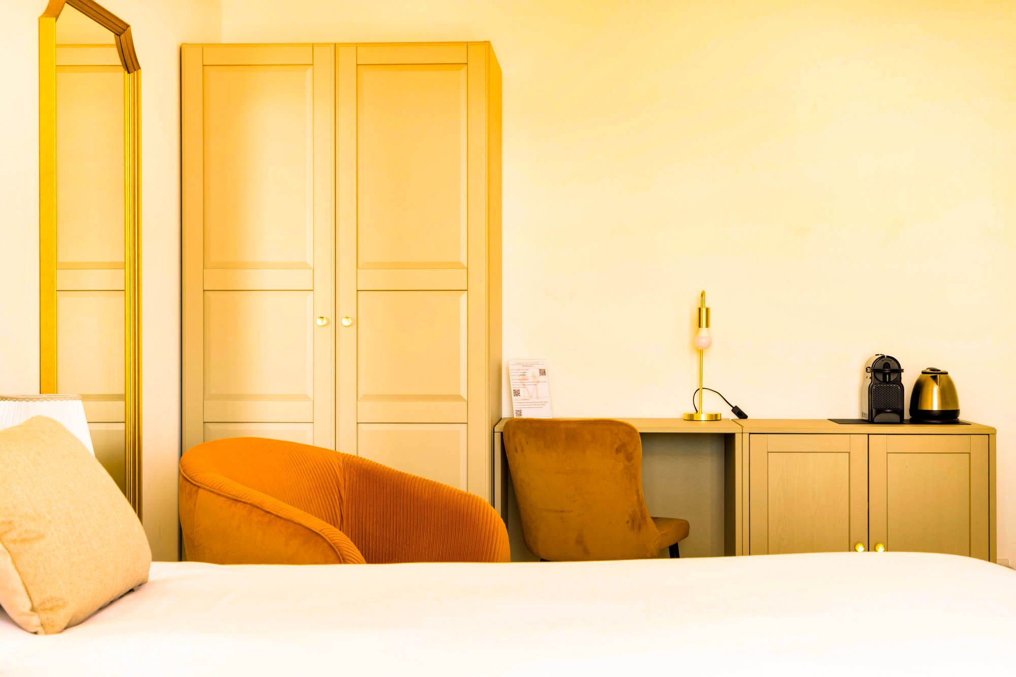 A hotel room with a bed, a desk, a chair, a wardrobe, and a lamp.