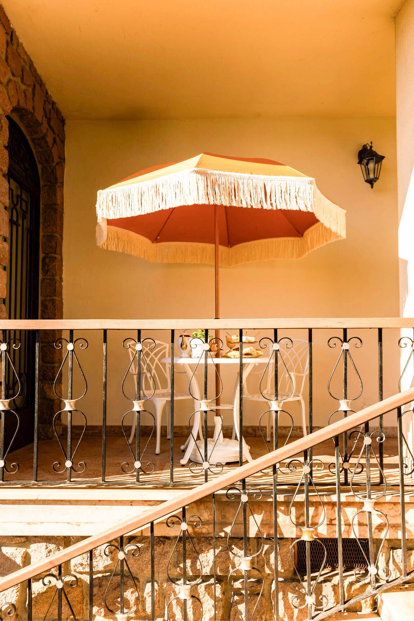 A balcony with a wrought iron railing, a table with chairs, and a large umbrella.
