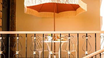 A balcony with a wrought iron railing, a table with chairs, and a large umbrella.