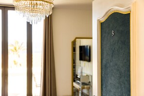 A room with a chandelier, a door with a number, and a mirror reflecting a TV. - Hotel Villa Martini (Ajaccio)
