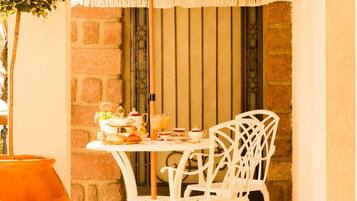 Une terrasse dallée de pierres, avec une table et des chaises, un parasol orange suspendu et une plante en pot.