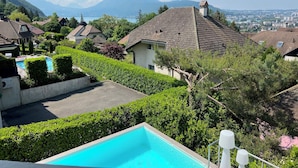 A residential area with a swimming pool, surrounded by well-maintained hedges and trees, with a view of distant mountains and a cityscape.