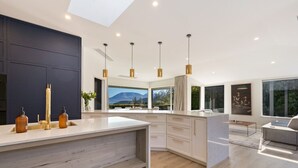 Una cocina moderna con una isla central, iluminación colgante y vistas a montañas a través de amplios ventanales.