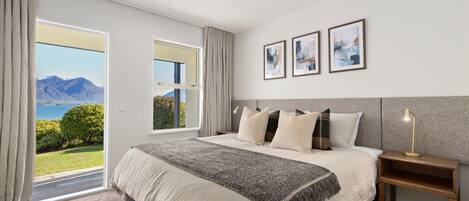 A bedroom with a large bed, a nightstand, and a view of the outdoors.