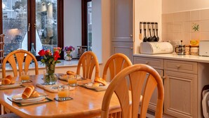 A dining area with a wooden table, chairs, breakfast items, and a view through large windows. - Apartment in Falmouth Near Beaches & Harbour (Falmouth)