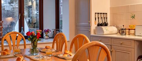 A dining area with a wooden table, chairs, breakfast items, and a view through large windows.