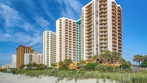 Un hotel a peu de platja amb diversos edificis alts, que disposa de balcons i una platja de sorra al primer pla.