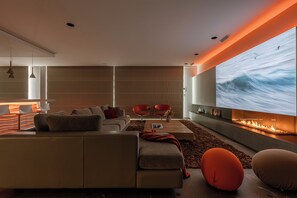 A modern living room with a large flat-screen TV, a sofa, two red chairs, and a fireplace.