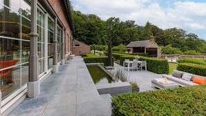Eine moderne Außenpatio mit Sitzgelegenheit, einem kleinen Wasserspiel und einem Backsteinhaus mit großen Fenstern.