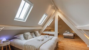 Ein Schlafzimmer mit Schräge, Dachfenstern, einem Bett mit weißer Bettwäsche, einem Nachttisch mit Lampe und Holzboden.