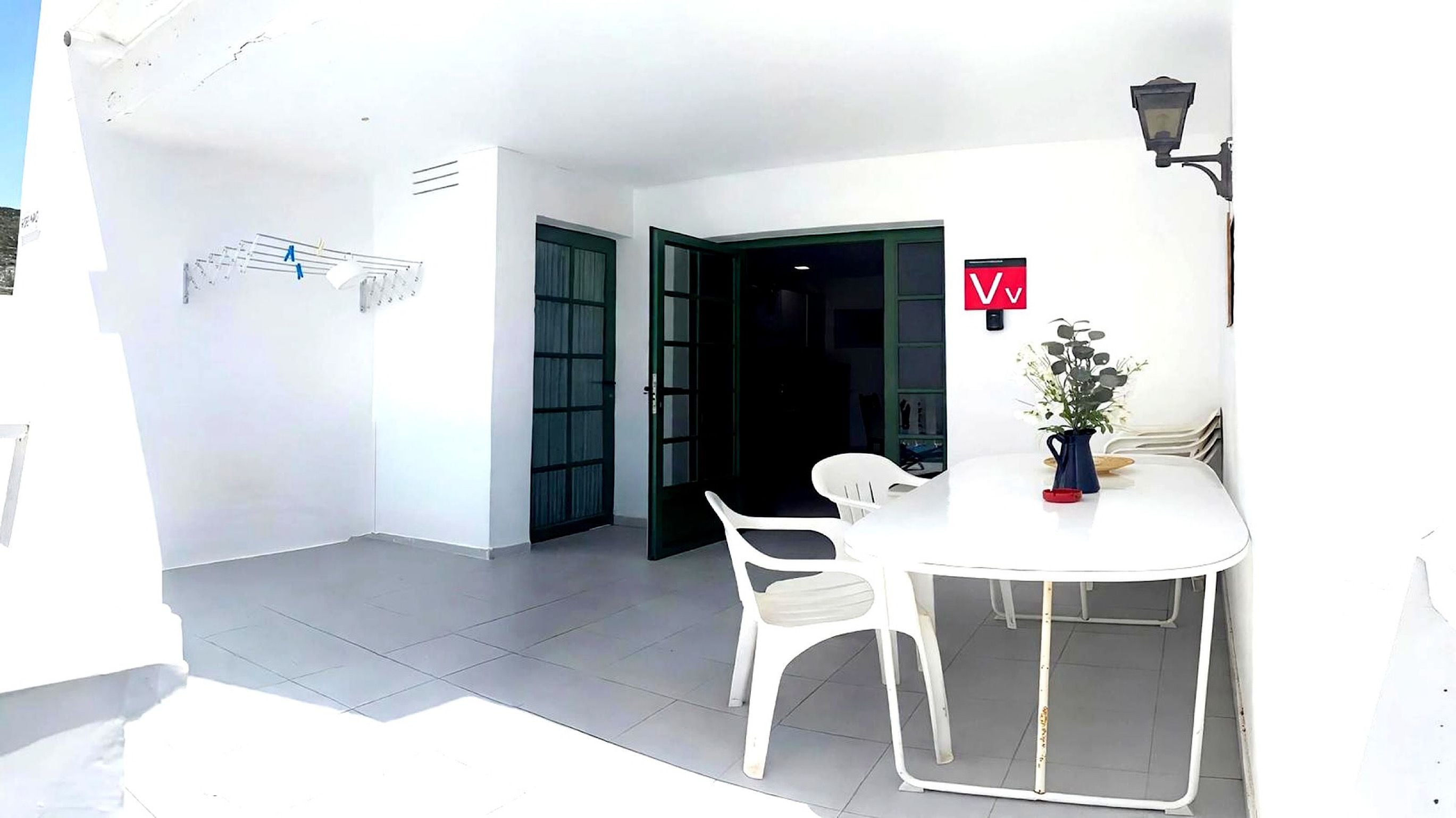 Una habitación blanca con una mesa redonda y dos sillas, una puerta y una lámpara fijada a la pared.