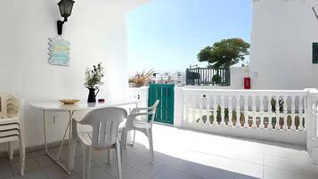A balcony with a white railing, a table with chairs, and a view of the sea.