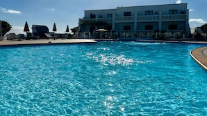 A swimming pool with lounge chairs and umbrellas, a multi-story building with balconies, and a clear blue sky. - Apartment Florencia With Pool & Wifi in Puerto del Carmen, Lanzarote (Tías)