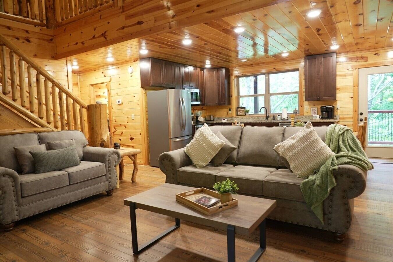 L’intérieur d’une cabane en rondins, avec un escalier, deux canapés, une table basse et un coin cuisine.
