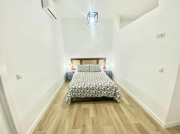 A bedroom with a bed, bedside tables, a hanging light fixture, and a wooden floor.