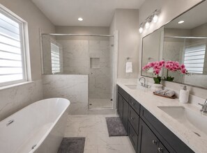 A modern bathroom with a freestanding bathtub, a walk-in shower, and a vanity with a large mirror.