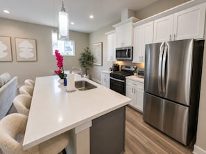 A modern kitchen with white cabinets, stainless steel appliances, a central island, and a dining area with chairs.