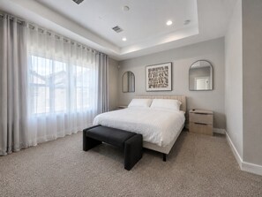A bedroom with a bed, a bench, a nightstand, a mirror, and a window with curtains.