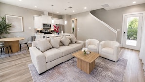 A modern living room with a sofa, chairs, a coffee table, and a kitchen in the background.