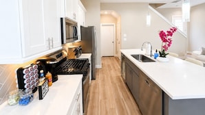 A modern kitchen with white cabinets, stainless steel appliances, and a wooden floor.