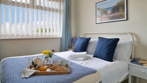 A neatly made bed with blue and white bedding, a tray with croissants, a teapot, and a vase of flowers.