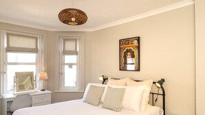 A bedroom with a bed, bedside lamps, a desk, and a window with blinds.