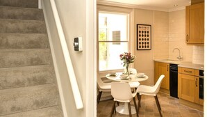 A modern kitchen with a dining area, featuring a staircase, a window with natural light, and a Bauhaus wall art piece.