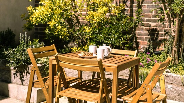 A wooden table with chairs, a plate of food, and a teapot and cup.