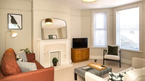 A living room with a fireplace, sofa, armchair, and a television.