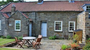 A stone house with a tiled roof, a front door, and a small porch area with potted plants. - Cottage in North York Moors Near Manor House (Middlesbrough)