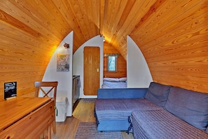 A cozy attic bedroom with wooden walls, a bed, a sofa, and a small desk.