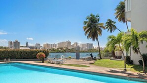 Una piscina con un paisaje urbano de fondo, palmeras y un césped bien cuidado.