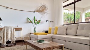 A modern living room with a beige sofa, a wooden coffee table, and a large window offering a view of greenery outside. - Villa Branca (Ponta do Sol)