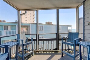 A balcony with blue chairs, a view of a blue building, and a clear sky.