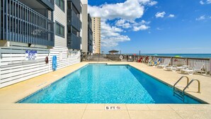 A swimming pool with a 5 ft depth limit sign, adjacent to a beach with lounge chairs and umbrellas. - Sea Oaks 308 - Two Bedroom, Two Bath Corner Oceanfront Condo (Garden City Beach)